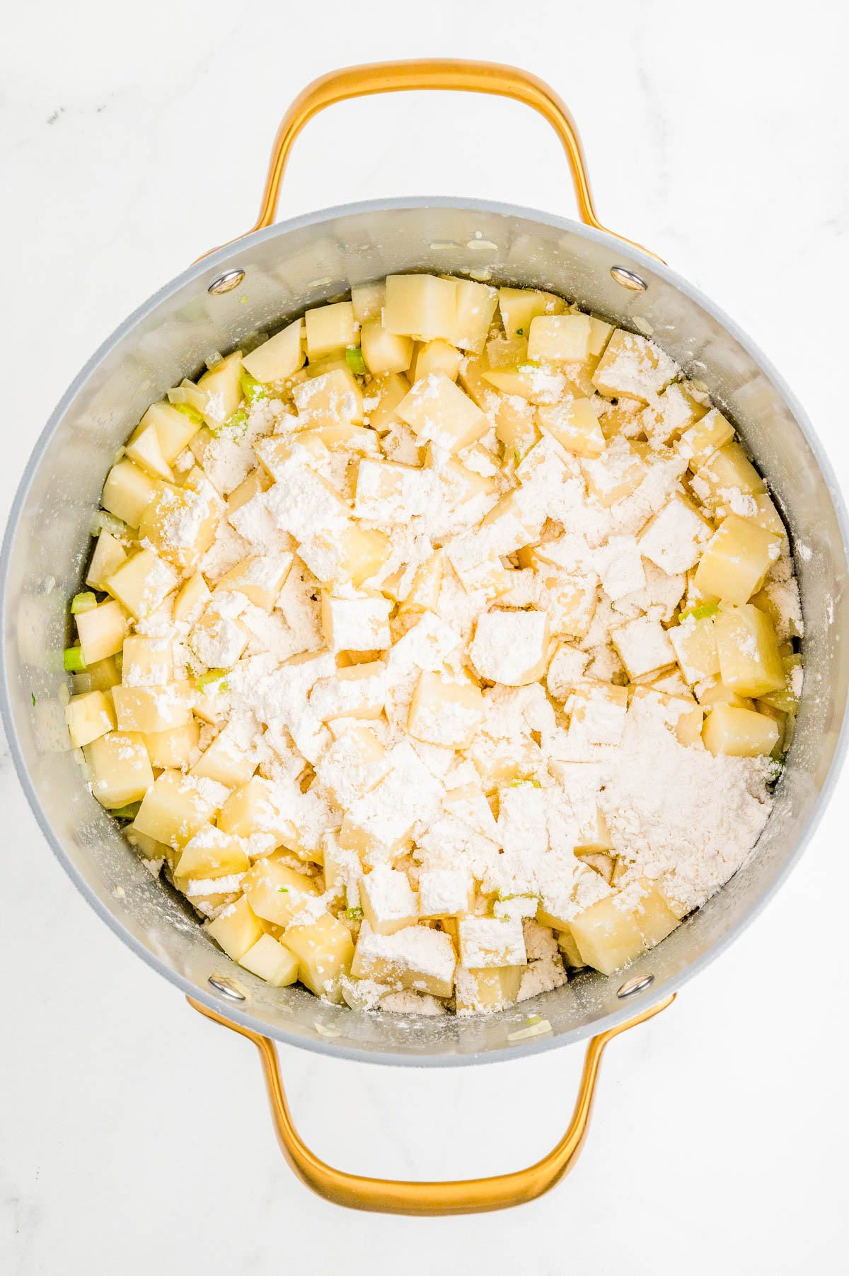 A pot filled with diced potatoes and flour, ready to be mixed, on a white background.