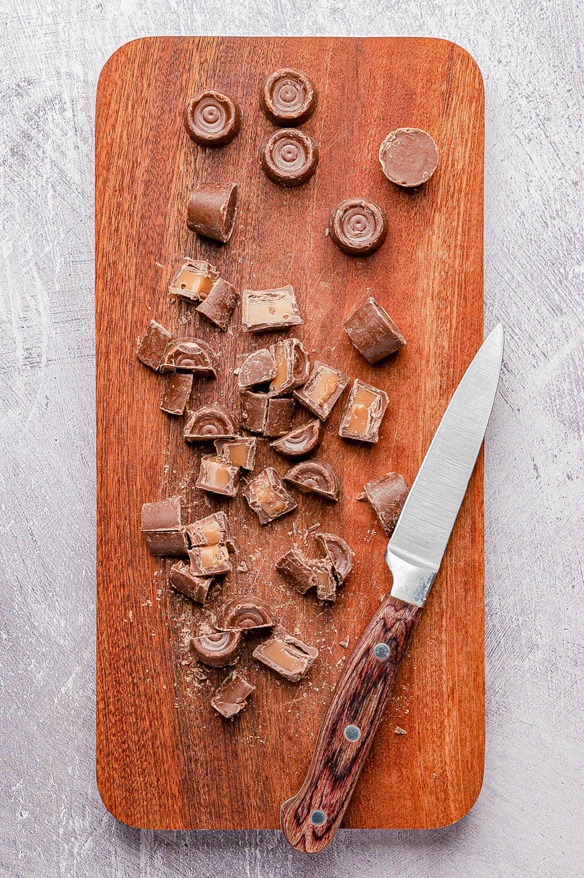 A wooden cutting board with a knife and several pieces of sliced chocolate candy, some with caramel filling visible.