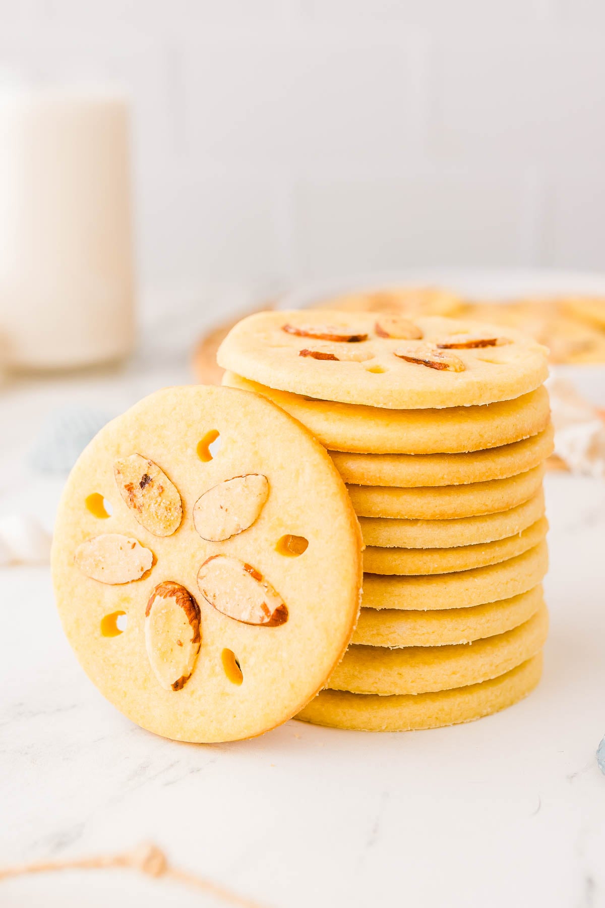 A stack of round cookies with almond slices arranged in a flower pattern on each, placed on a white surface.