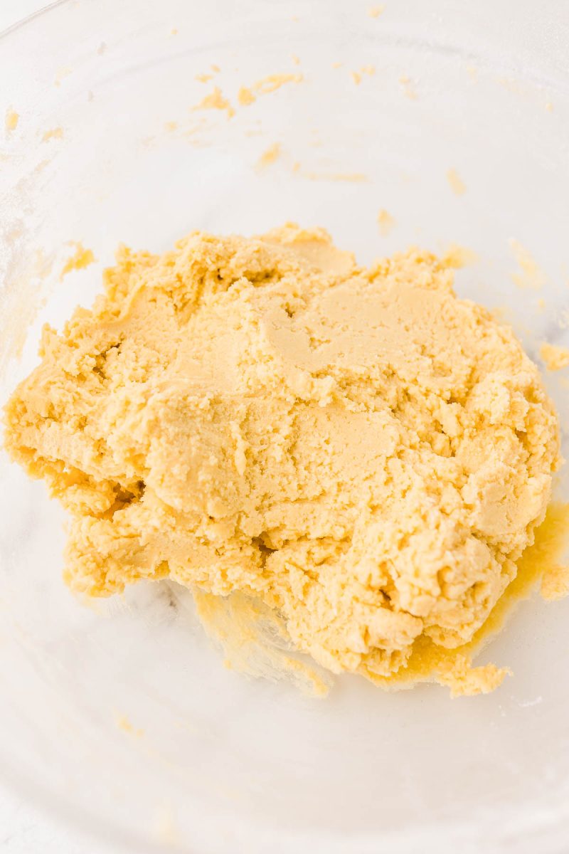 A clear glass bowl filled with yellow cookie dough mixture.
