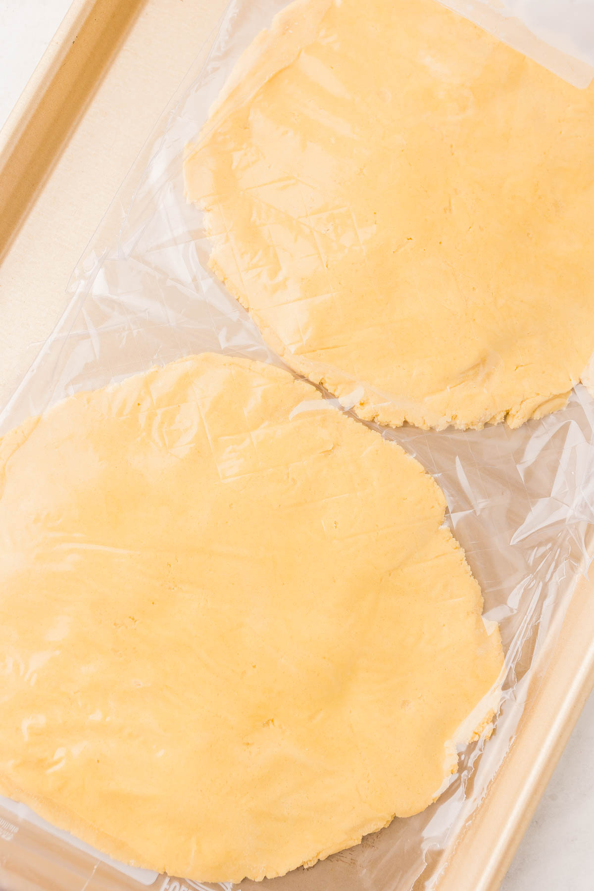 Two discs of raw pastry dough wrapped in plastic wrap are placed on a baking sheet.