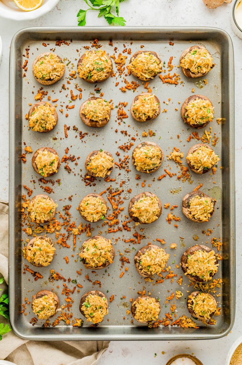 A baking sheet with several stuffed mushrooms topped with a golden breadcrumb mixture, arranged in neat rows.