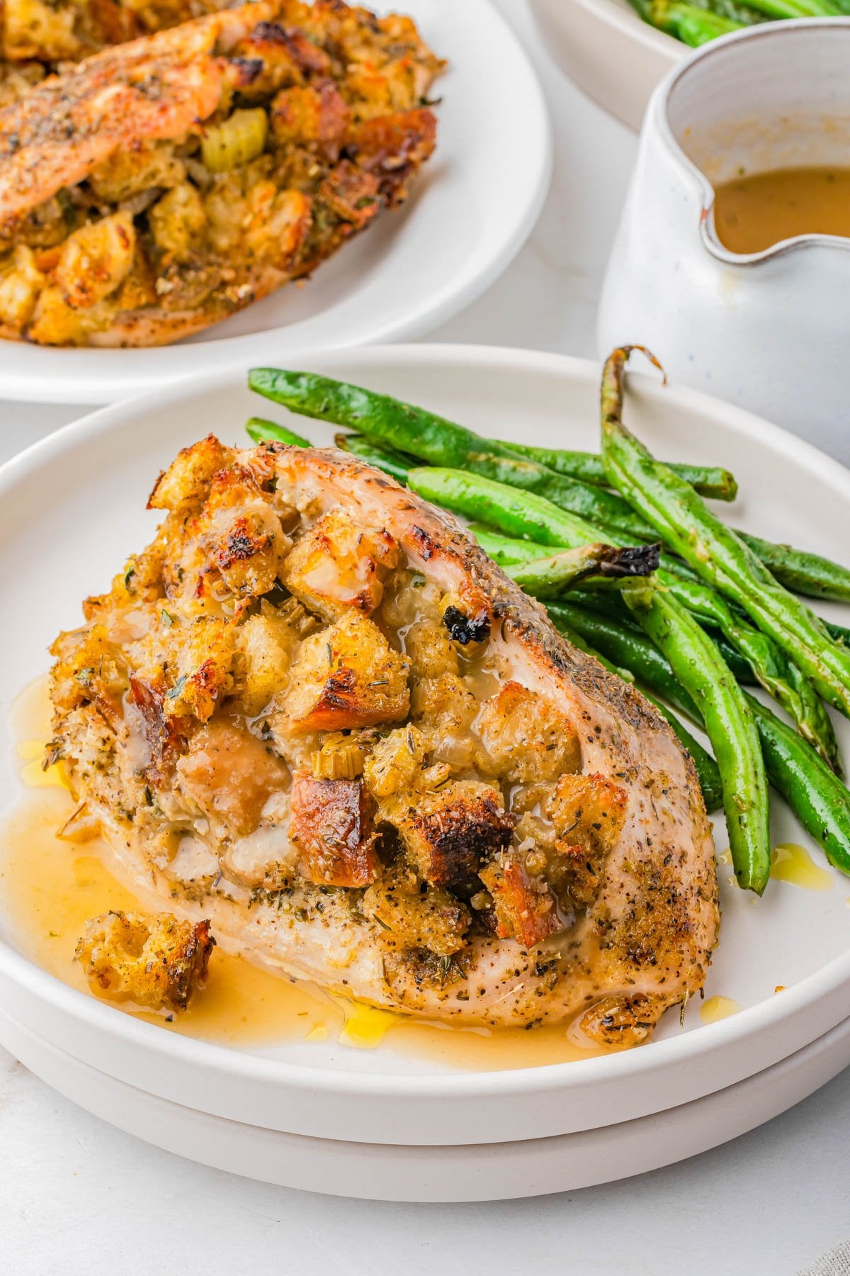 A plate with stuffed chicken breast topped with gravy, served alongside sautรฉed green beans.