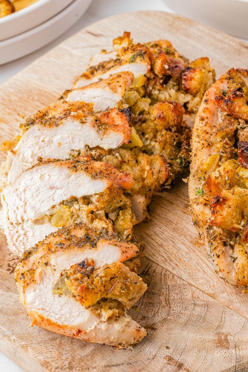Sliced stuffed chicken breast with seasoned bread stuffing on a wooden cutting board.