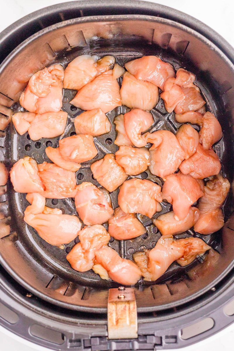 Raw, cubed chicken pieces arranged in a single layer inside an air fryer basket, ready to be cooked.