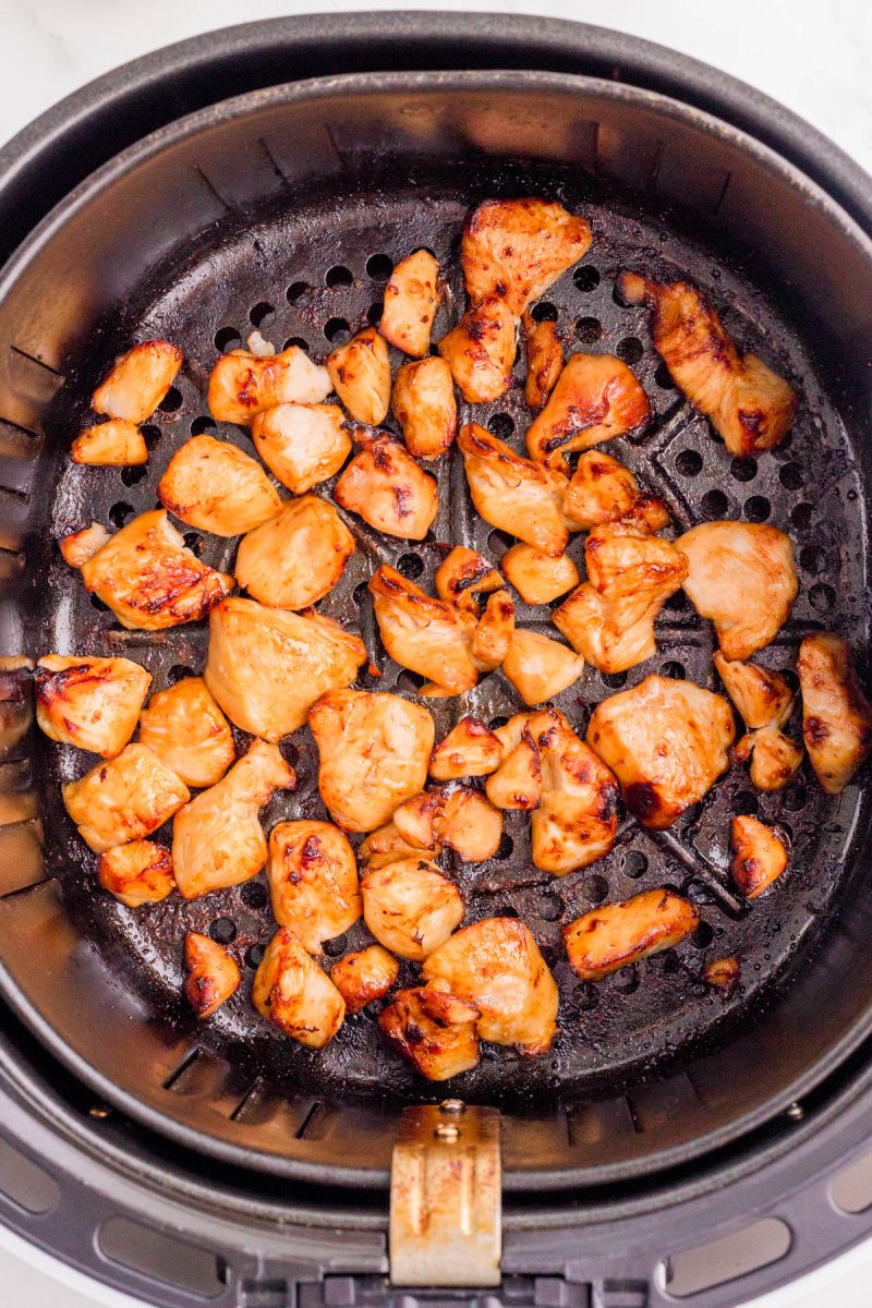 Cooked chicken pieces in an air fryer basket, lightly browned and evenly distributed across the perforated base.