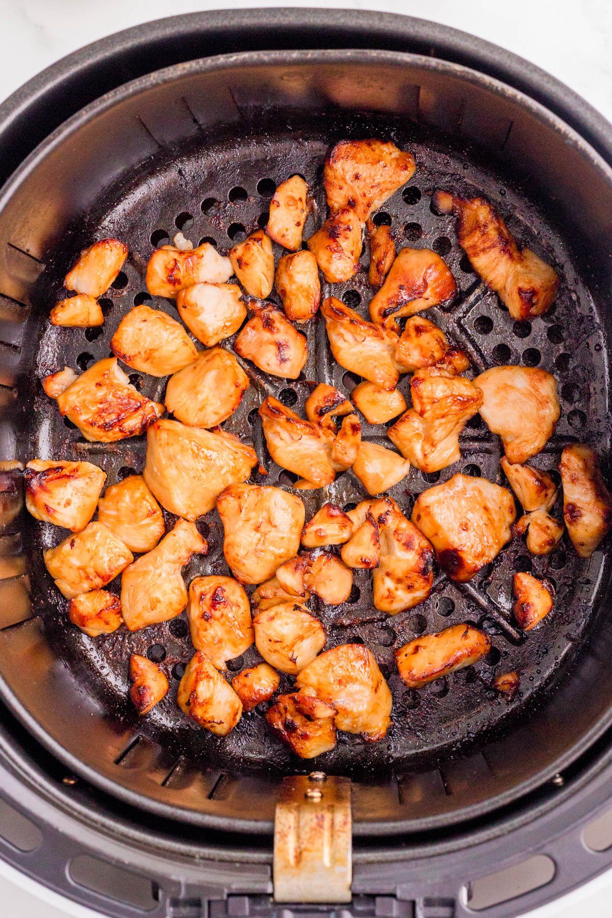 Cooked chicken pieces in an air fryer basket, lightly browned and evenly distributed across the perforated base.