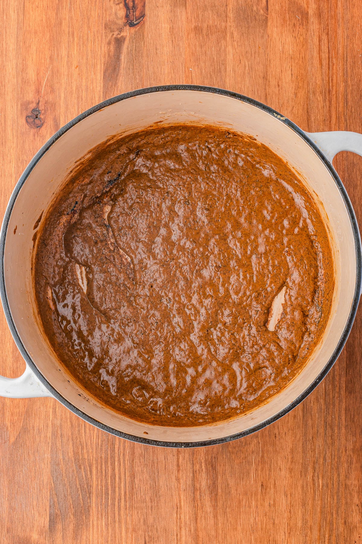 A large pot containing a thick, brown sauce or stew sits on a wooden surface.