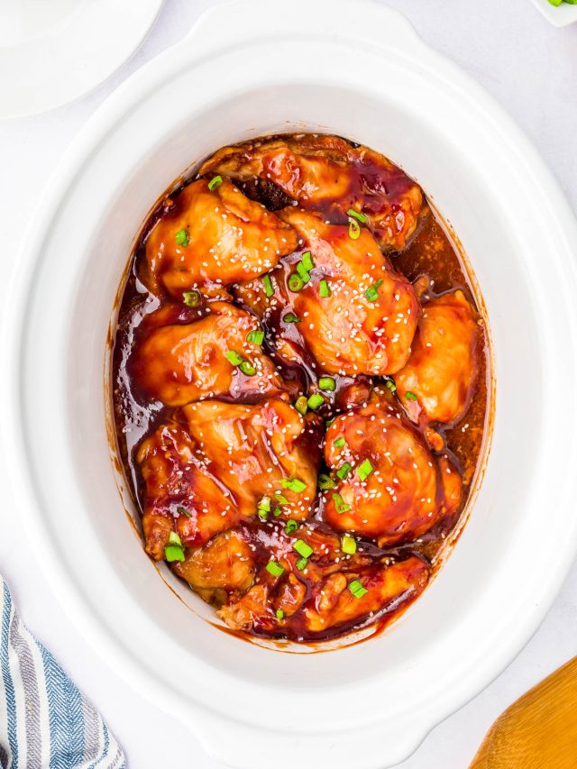 Chicken thighs coated in a glossy brown sauce, garnished with chopped green onions, in a white slow cooker.