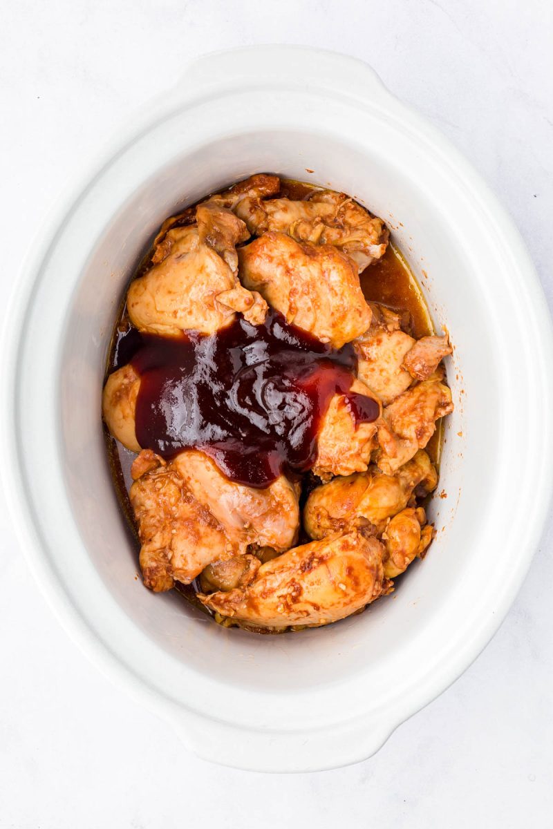 Cooked chicken pieces topped with barbecue sauce inside a white slow cooker, photographed from above.