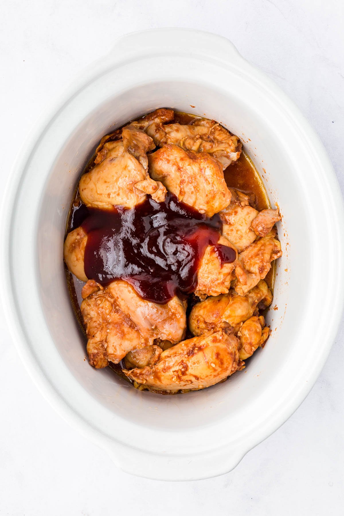 Cooked chicken pieces topped with barbecue sauce inside a white slow cooker, photographed from above.