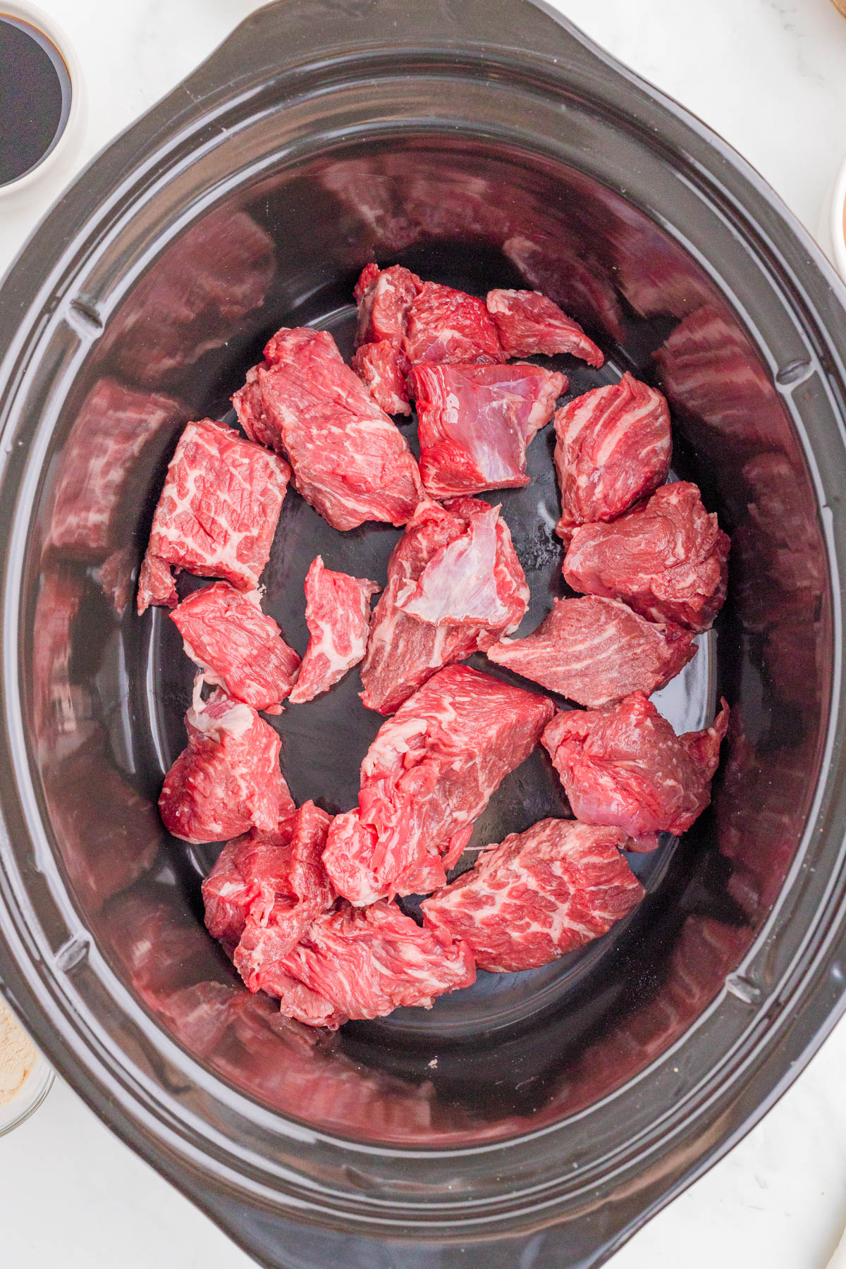 Chunks of raw beef placed in the bottom of a black slow cooker.