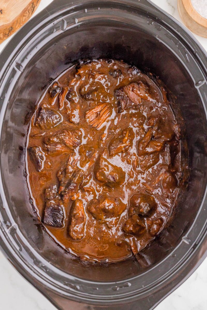 Chunks of beef in a thick brown sauce inside a black slow cooker, with some sauce residue on the sides.