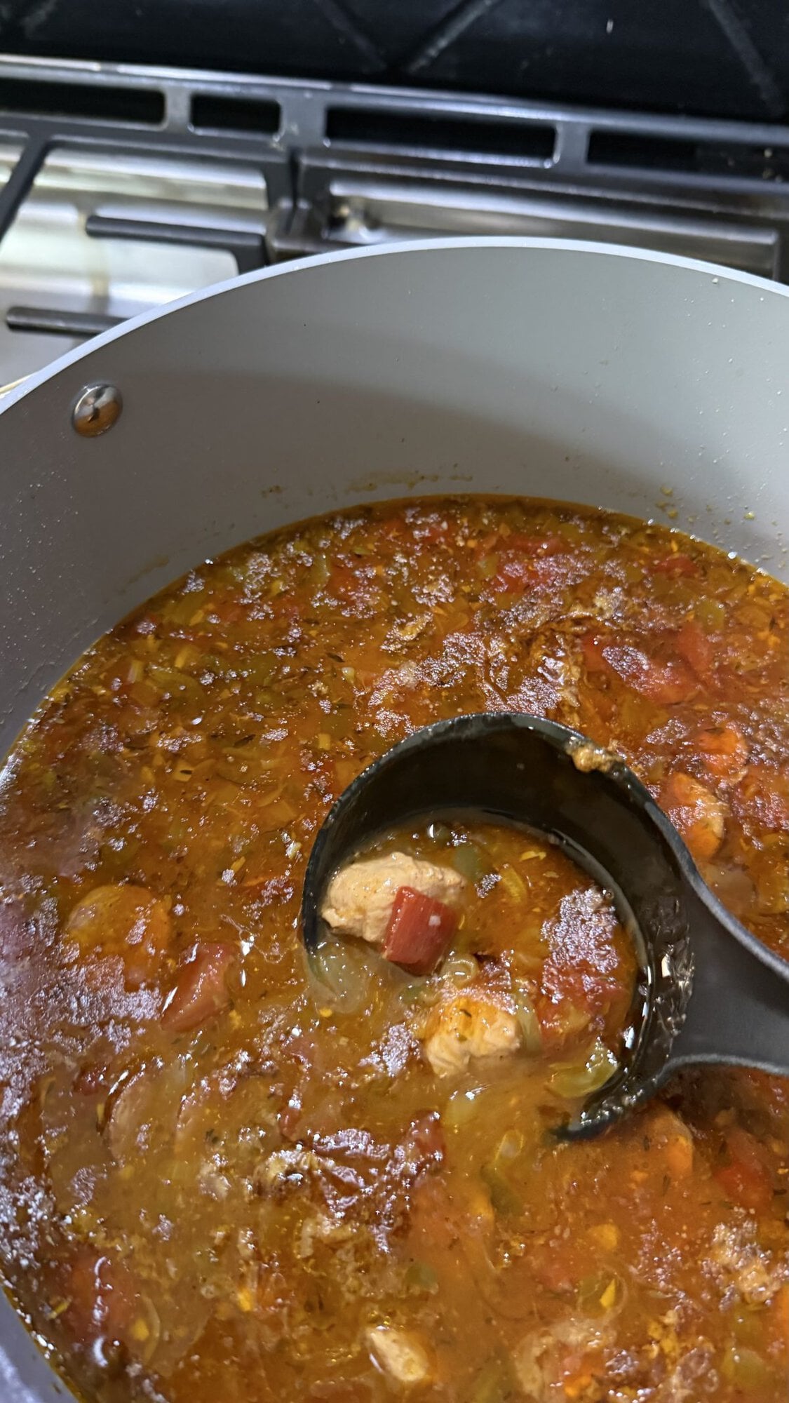 A pot of stew with vegetables and meat pieces simmers on a stove, with a black ladle lifting a portion from the mixture.