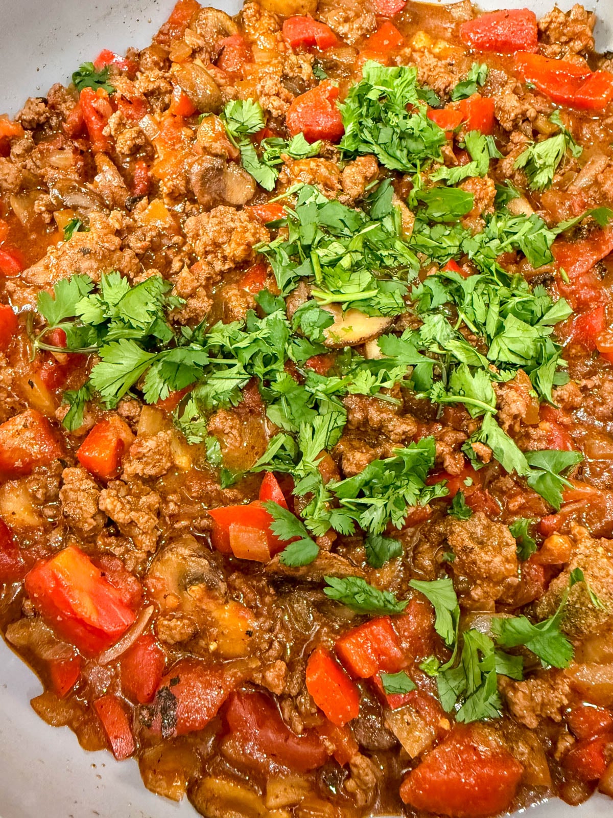 A close-up of a cooked ground meat dish mixed with chopped red bell peppers, onions, and tomatoes, topped with fresh cilantro.
