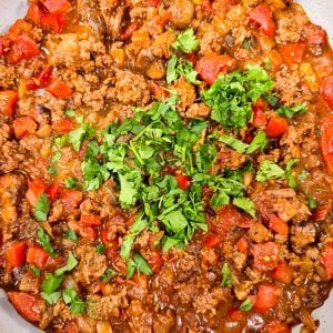 A skillet filled with cooked ground meat, diced red peppers, tomatoes, and onions, topped with fresh chopped cilantro.