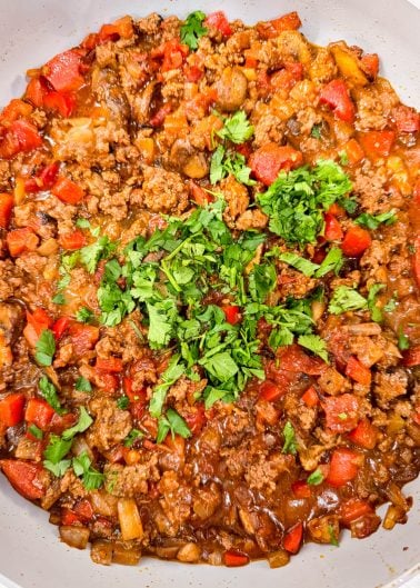 A skillet filled with cooked ground meat, diced red peppers, tomatoes, and onions, topped with fresh chopped cilantro.