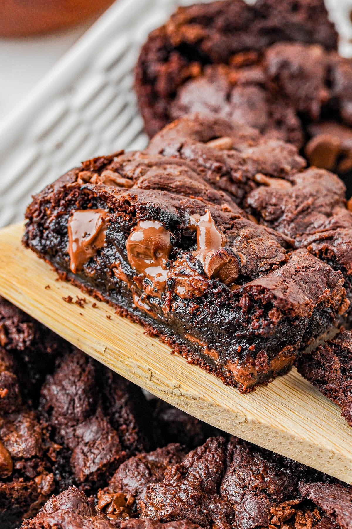 A close-up of a gooey chocolate brownie with melted chocolate chunks being lifted from a tray with a wooden spatula.
