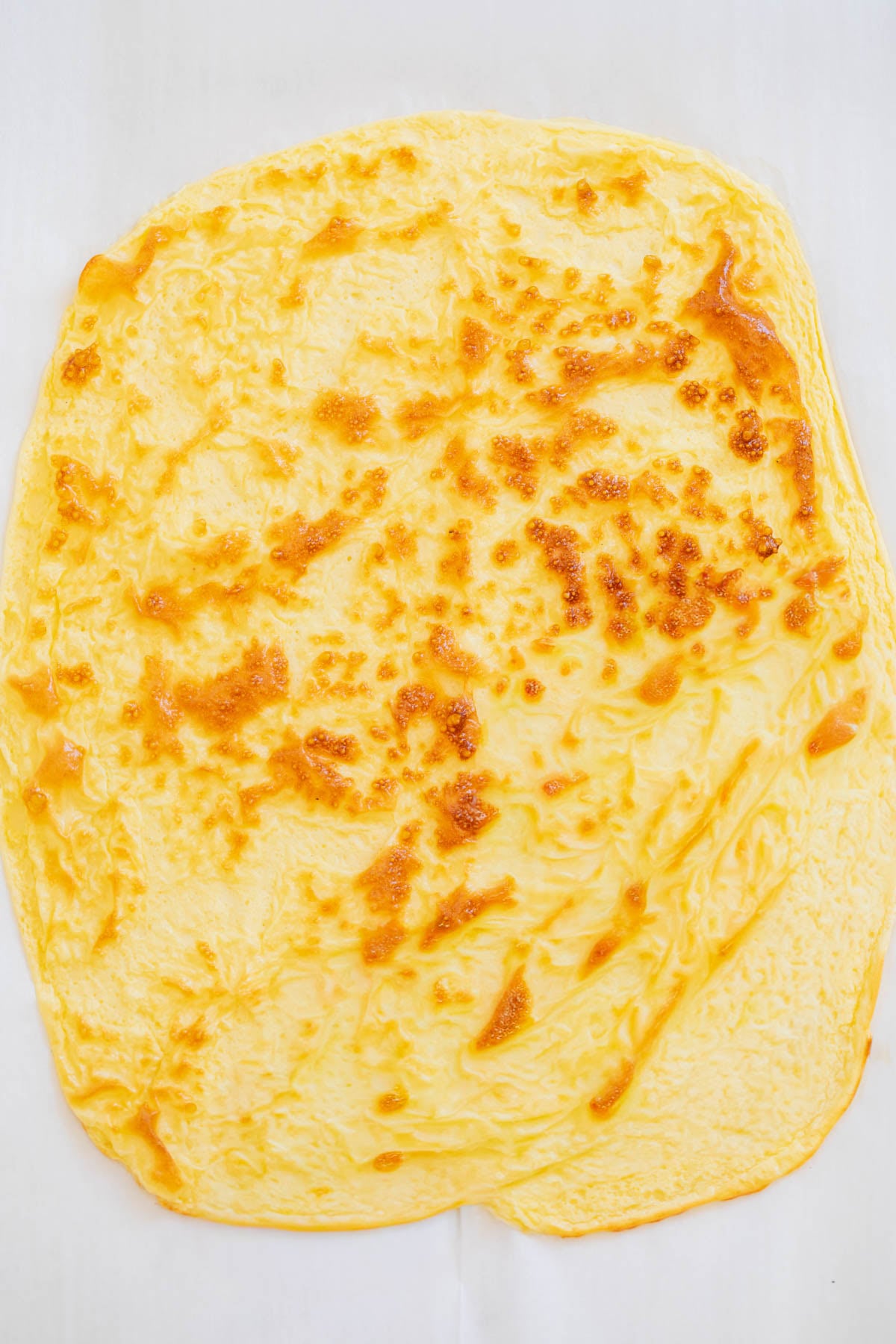 A large, thin sheet of cooked egg with a slightly browned, uneven surface on a white background.