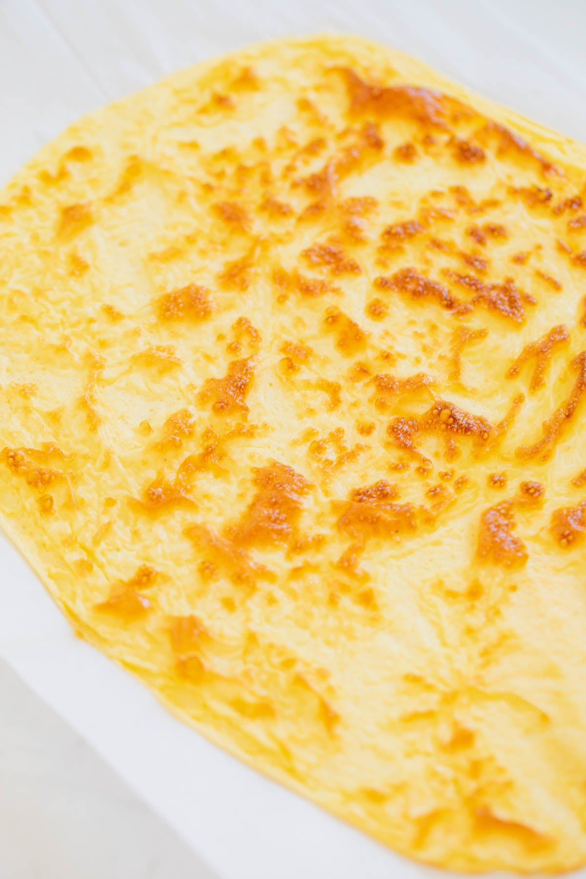 A sheet of baked egg mixture with a slightly browned, uneven surface, laid flat on parchment paper.