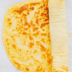 A cooked yellow egg wrap partially rolled up on a sheet of parchment paper.