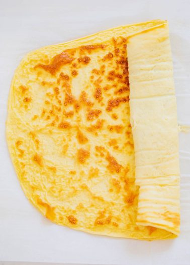 A cooked yellow egg wrap partially rolled up on a sheet of parchment paper.