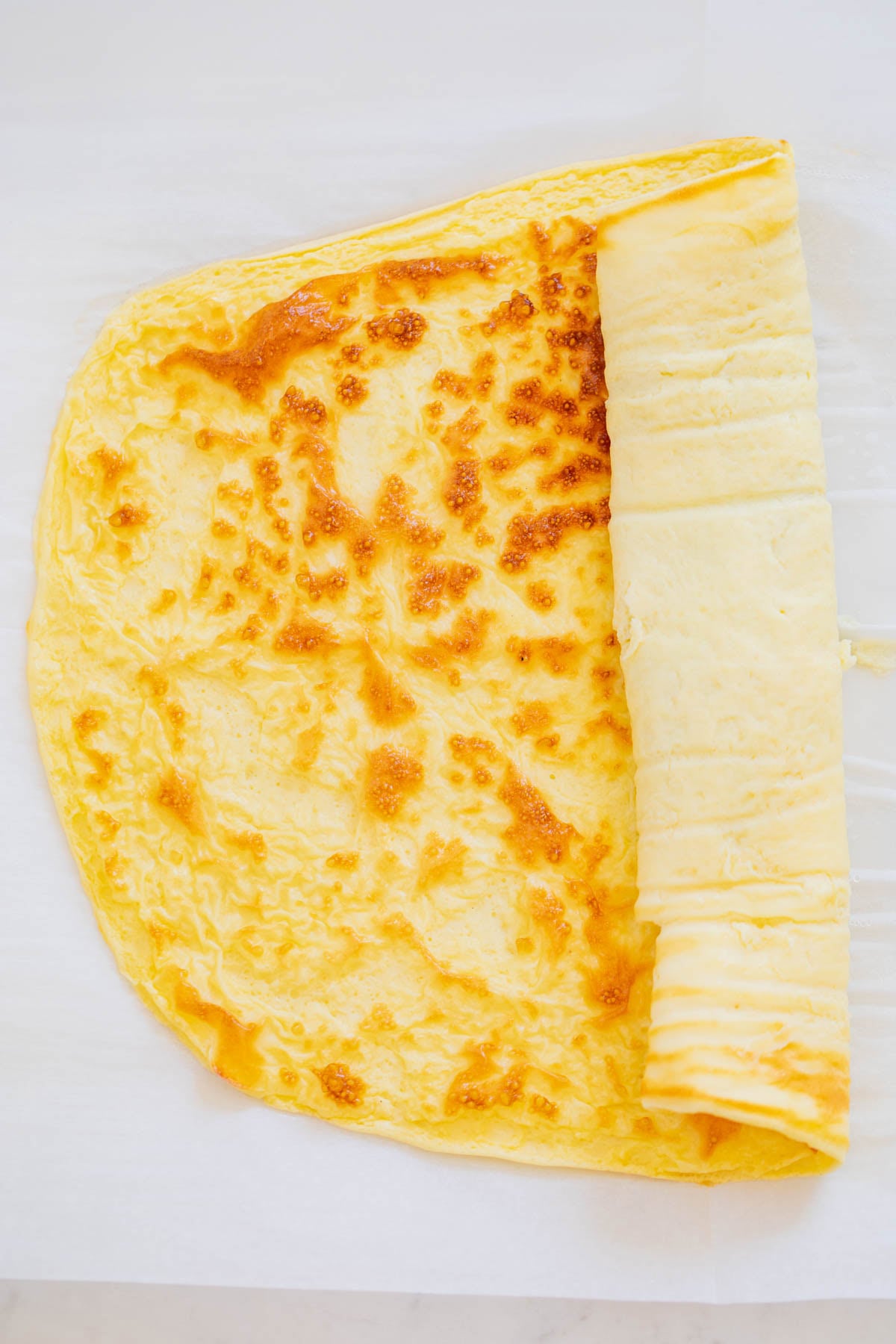 A cooked yellow egg wrap partially rolled up on a sheet of parchment paper.