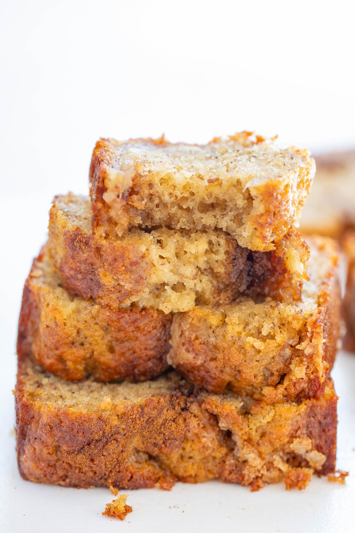 Four slices of banana bread are stacked on top of each other, with the top slice partially eaten, showing a moist, dense texture.