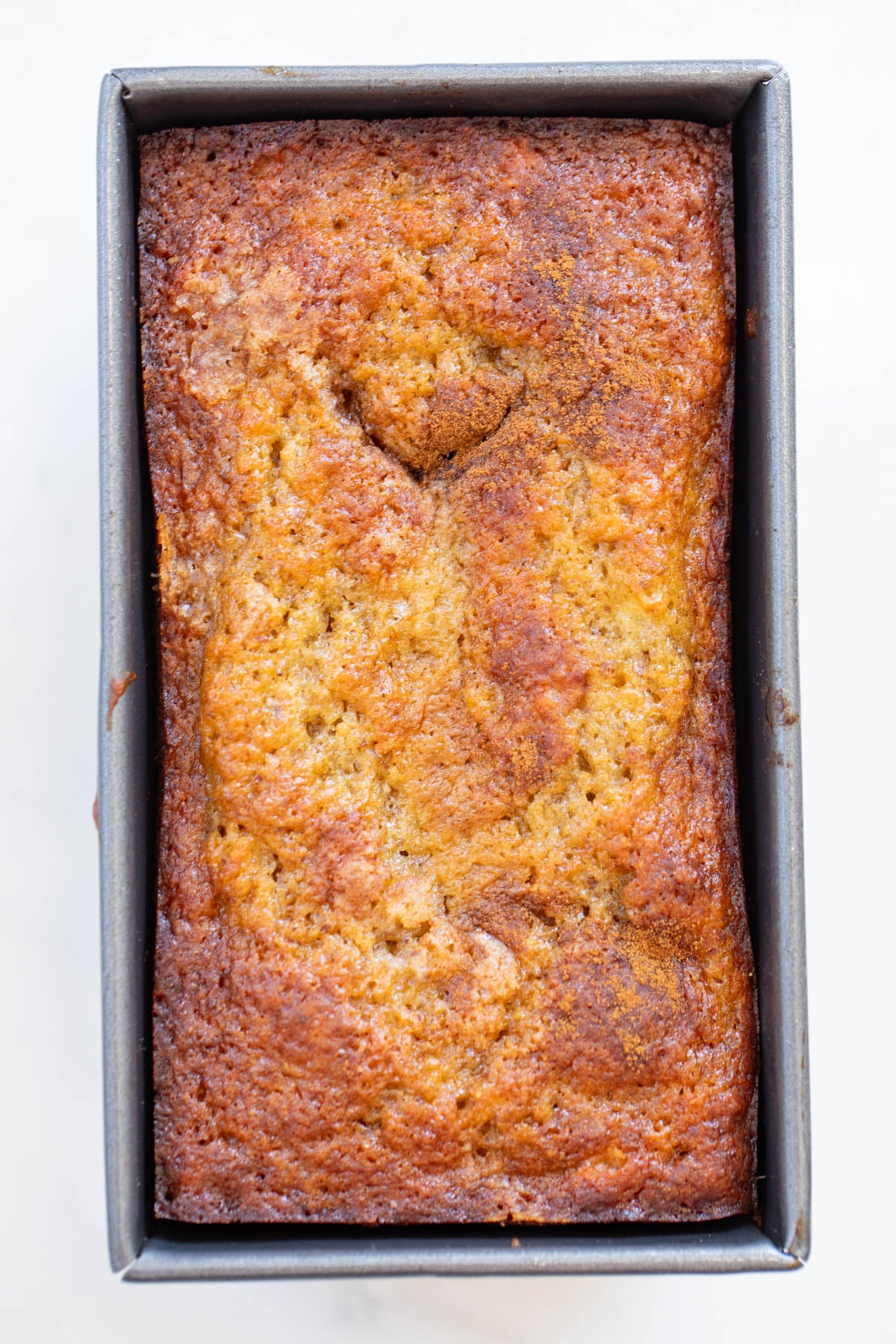 A loaf of baked banana bread in a rectangular metal pan, shown from above on a white background.