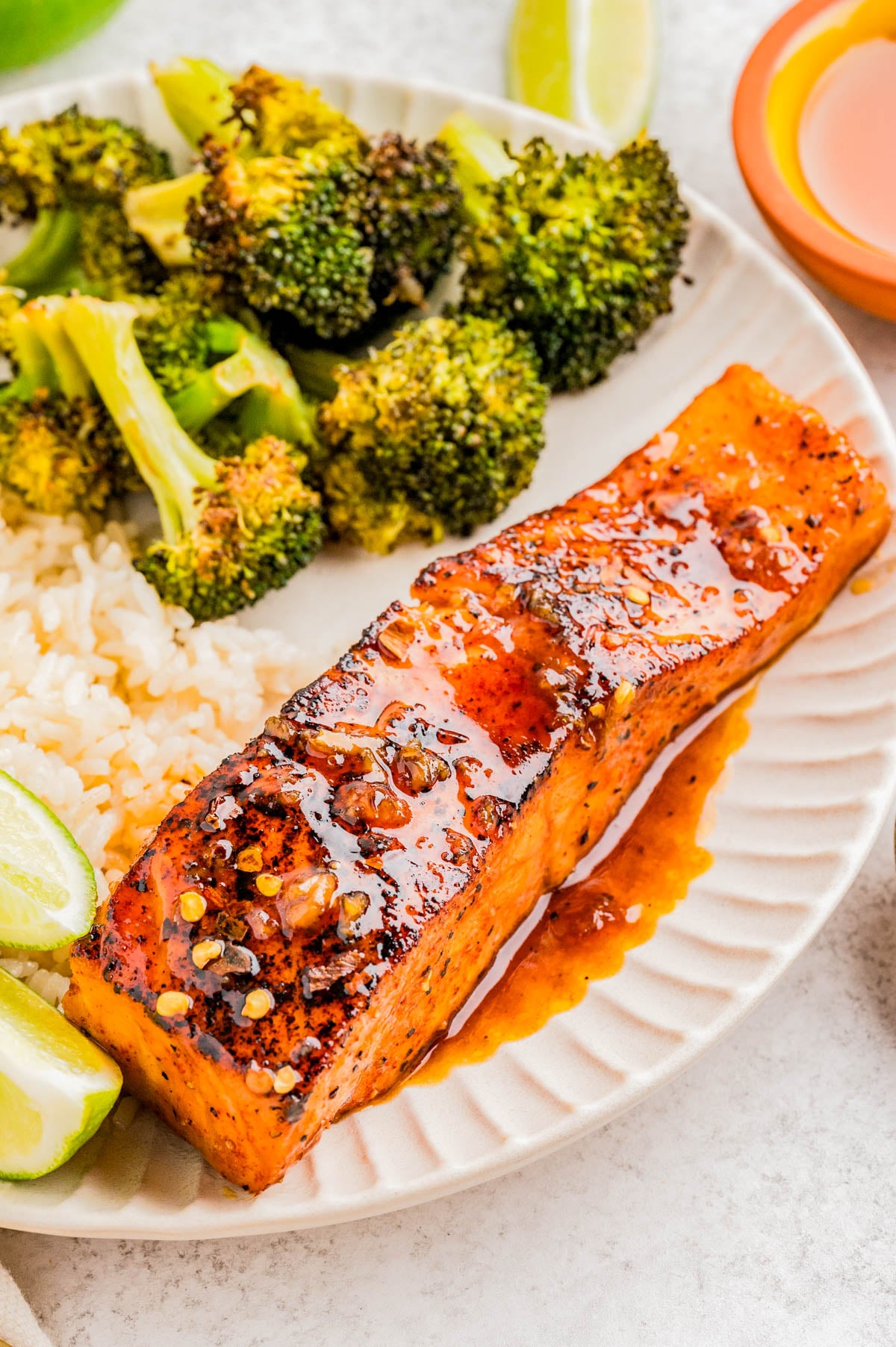 A plate with a glazed salmon fillet, steamed broccoli, white rice, and lime wedges.