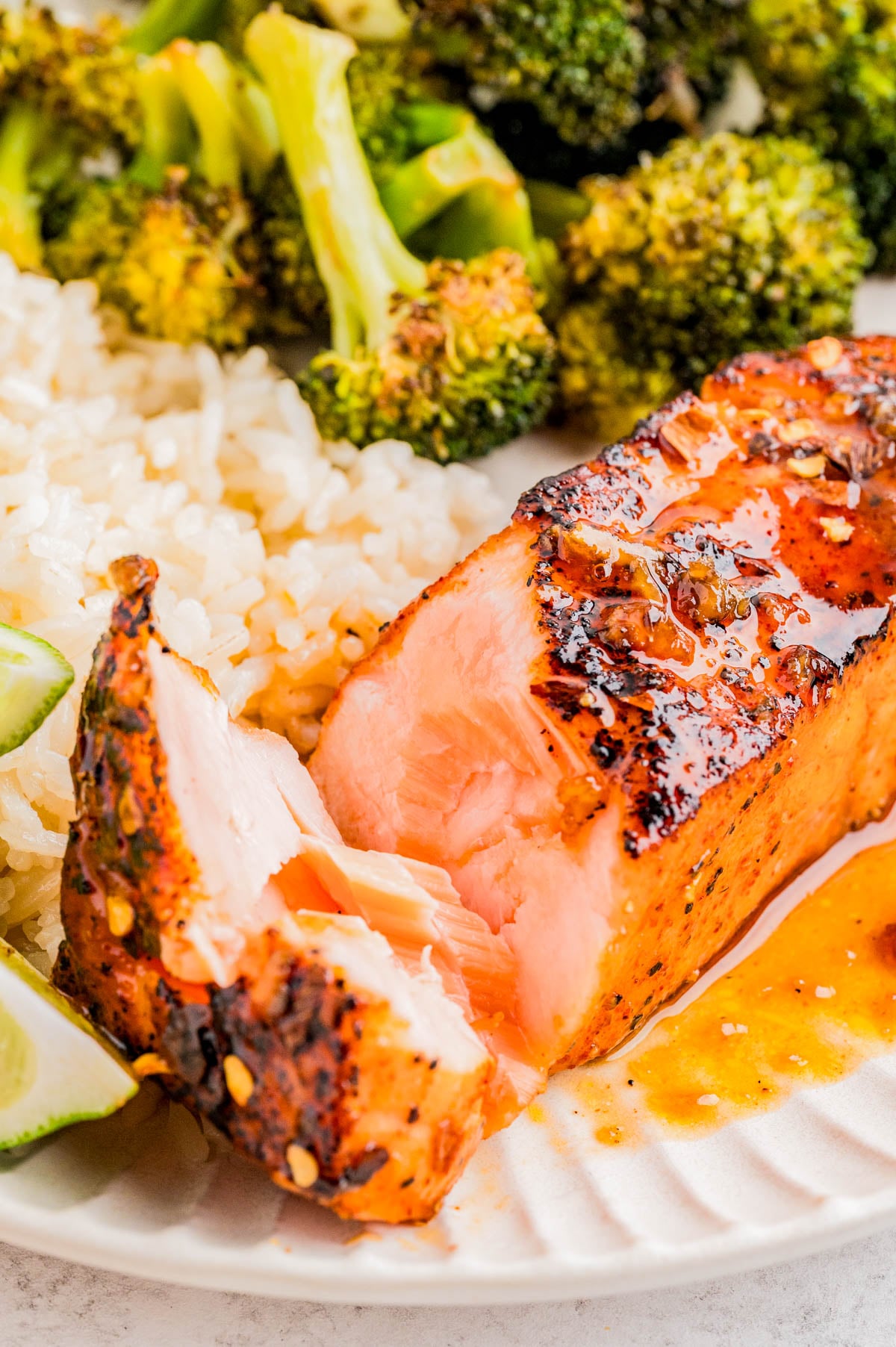 A plate with grilled salmon, white rice, broccoli, and a lime wedge. The salmon is partially cut to show its tender, flaky interior.