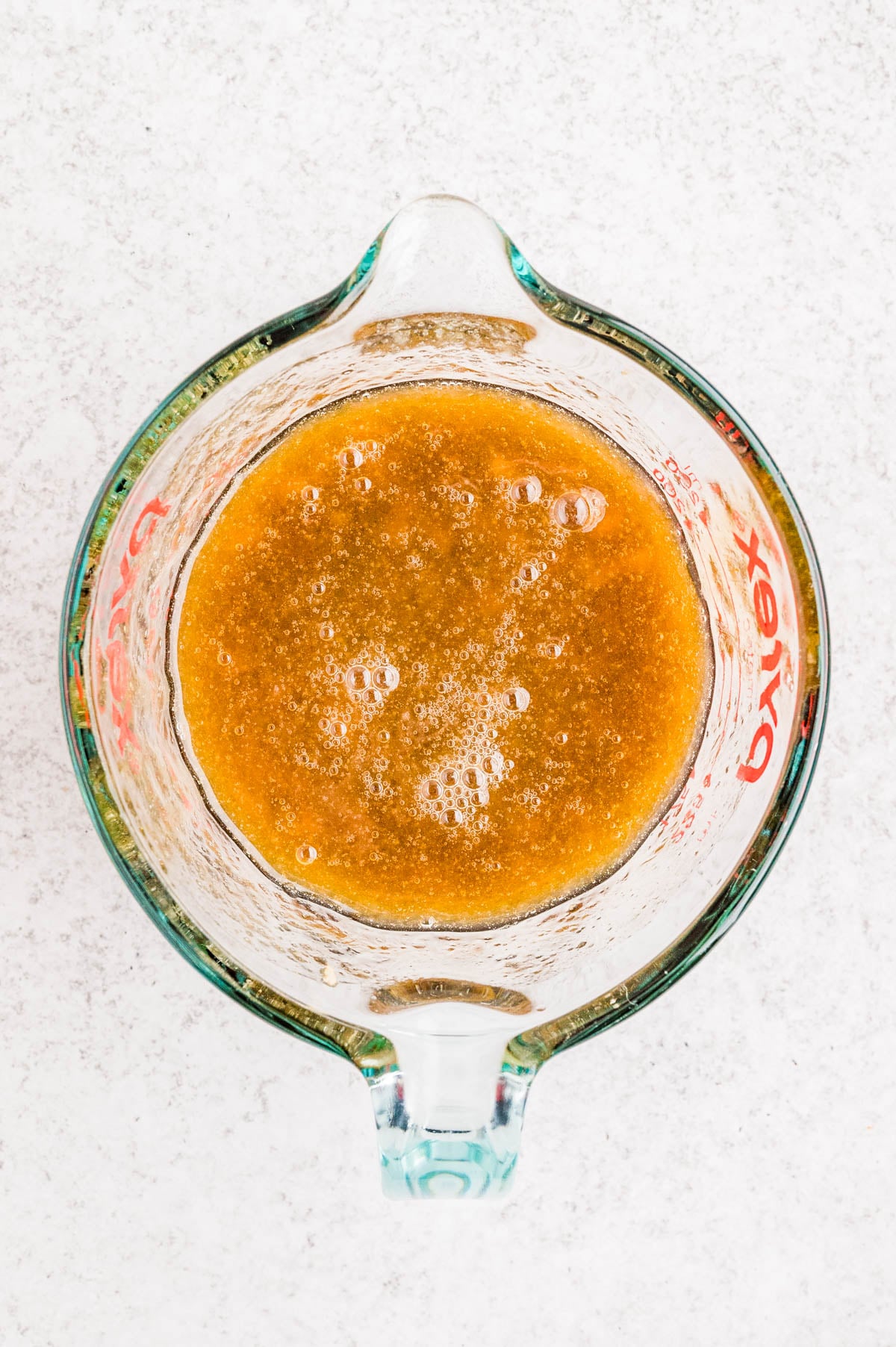 Overhead view of a glass Pyrex measuring cup filled with a foamy, brown liquid mixture on a light surface.