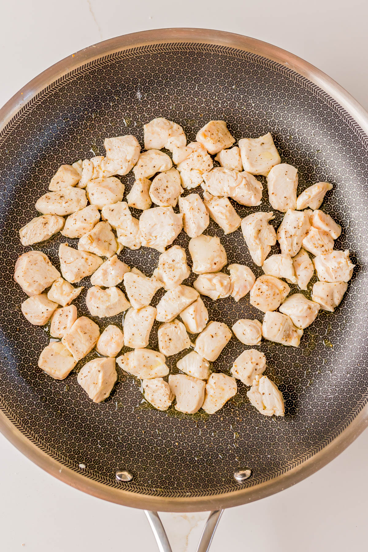 Diced chicken pieces cooking in a nonstick frying pan on a stovetop.