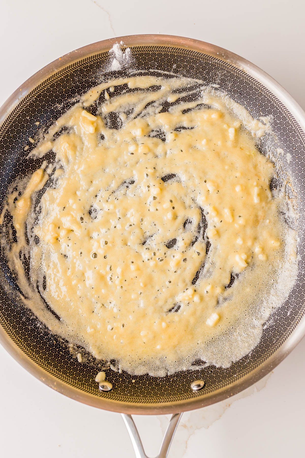 A frying pan with a mixture of melted butter and flour being cooked, forming the base of a roux on a stovetop.