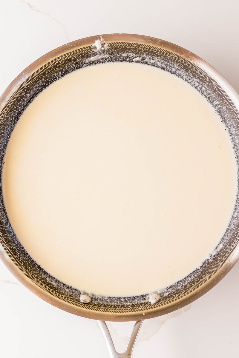 A stainless steel pan filled with a light-colored cream sauce, viewed from above on a white surface.