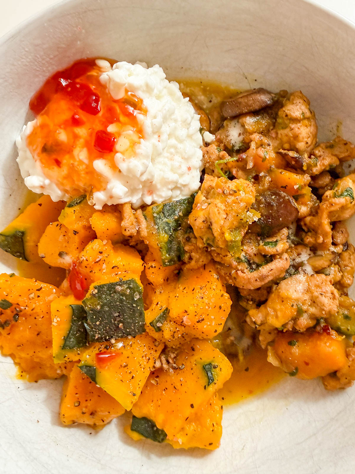 A bowl with cooked chicken and mushrooms, sliced yellow squash with black pepper, and a scoop of cottage cheese topped with red sauce.