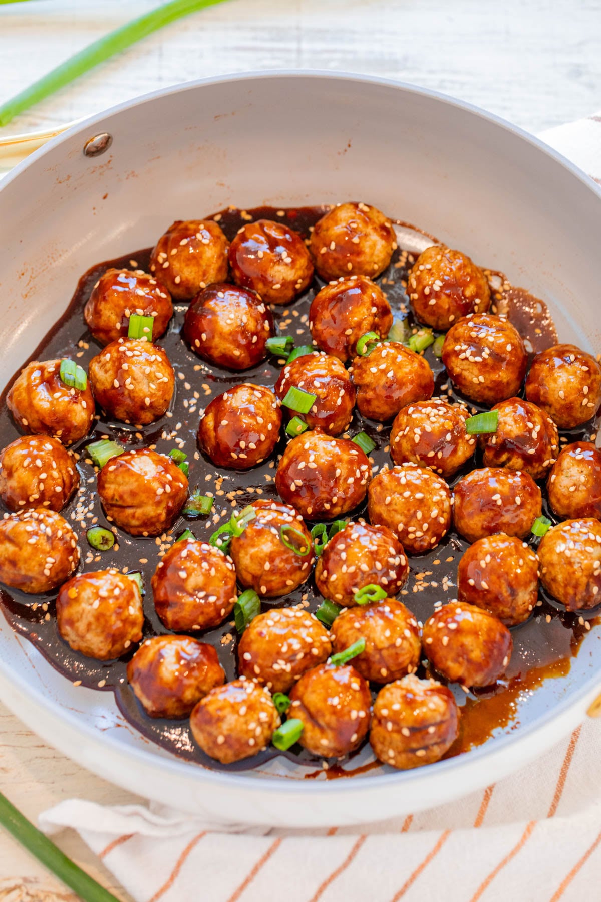 A pan filled with glazed meatballs covered in sauce, garnished with sesame seeds and chopped green onions.