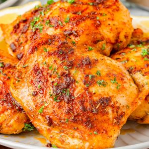 Close-up of baked, seasoned chicken thighs garnished with chopped herbs, served on a white plate.