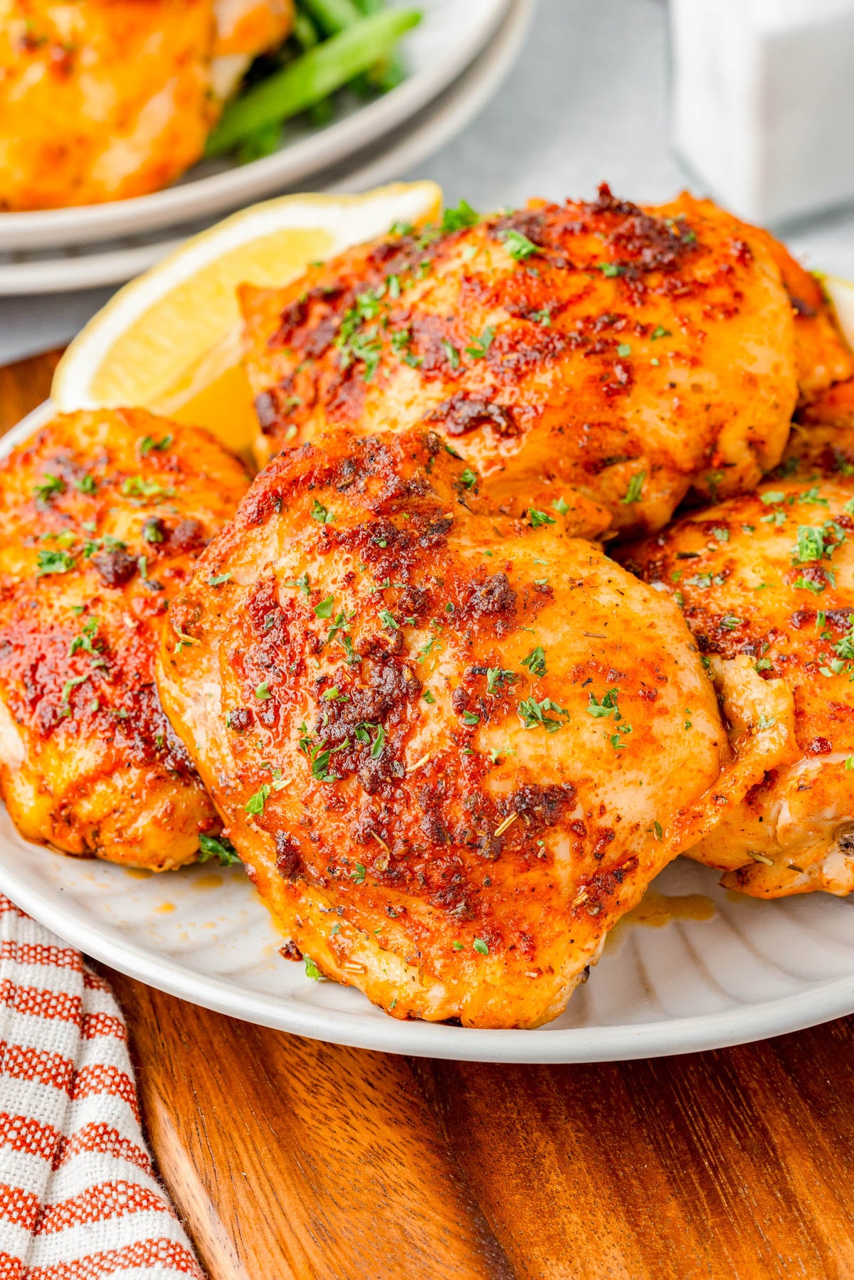 A plate of seasoned, baked chicken thighs garnished with chopped herbs, served with a lemon wedge on the side.