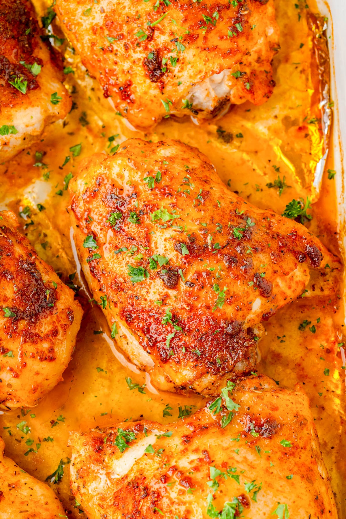 Close-up of baked chicken thighs with a golden, seasoned crust, garnished with chopped parsley and surrounded by a flavorful sauce.