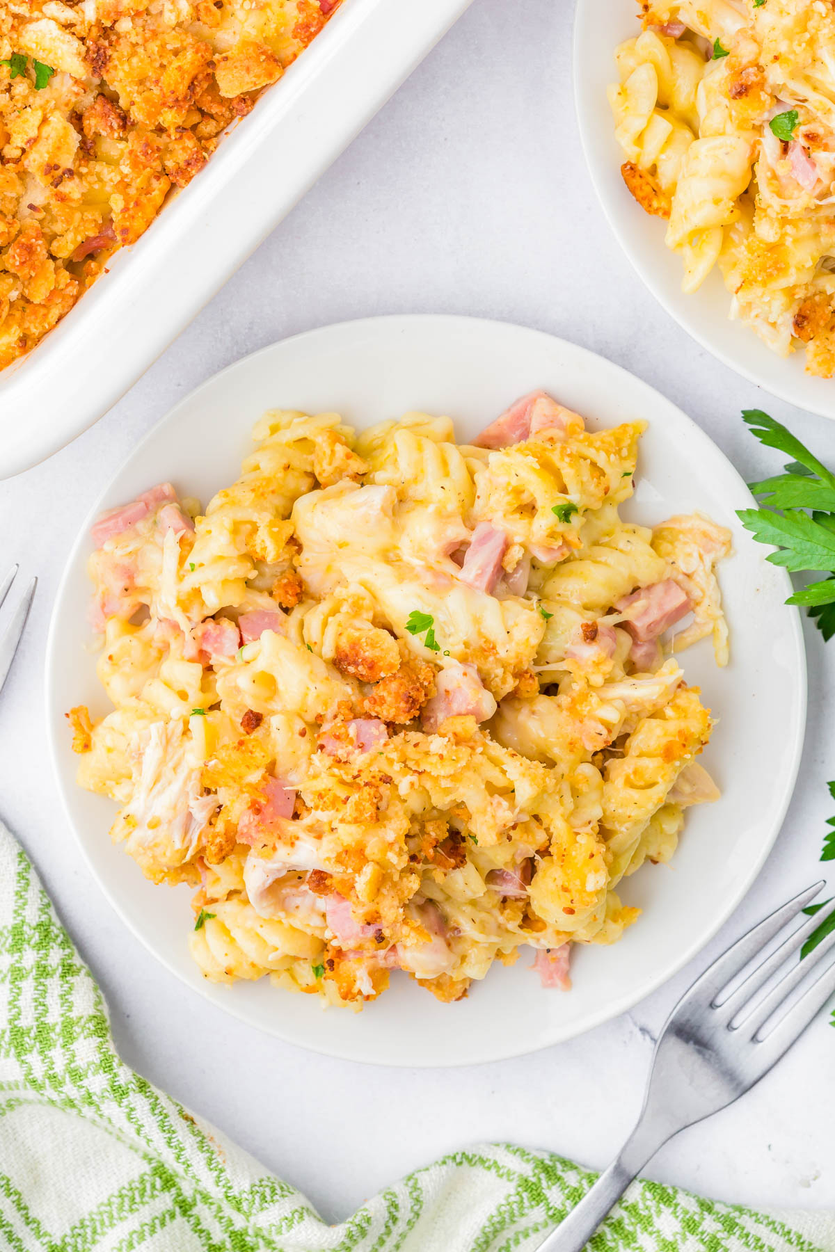 A plate of creamy pasta casserole with ham, topped with golden breadcrumbs, next to a fork and a green-patterned napkin.