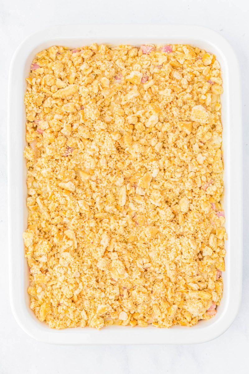 A white rectangular baking dish filled with a casserole topped with a golden, crumbly layer of crushed crackers.