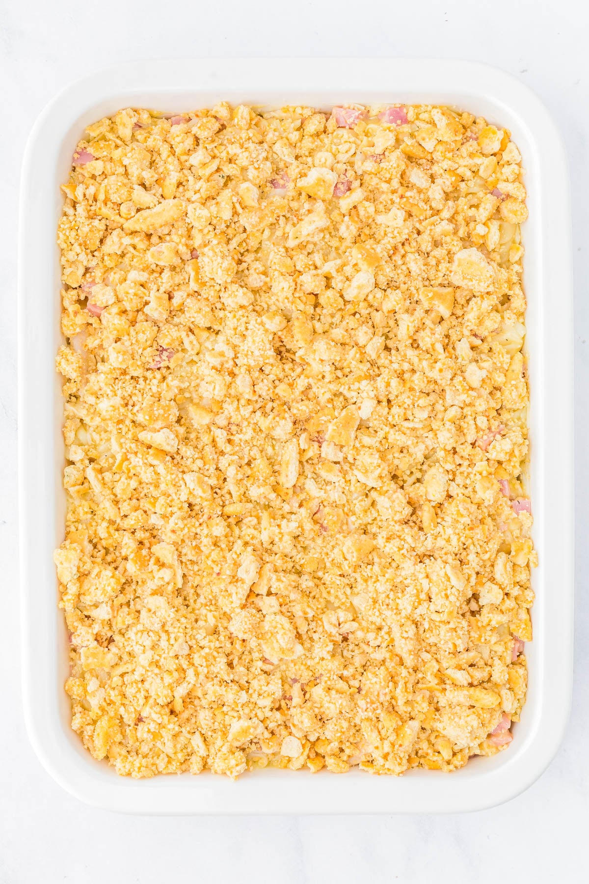 A white rectangular baking dish filled with a casserole topped with a golden, crumbly layer of crushed crackers.
