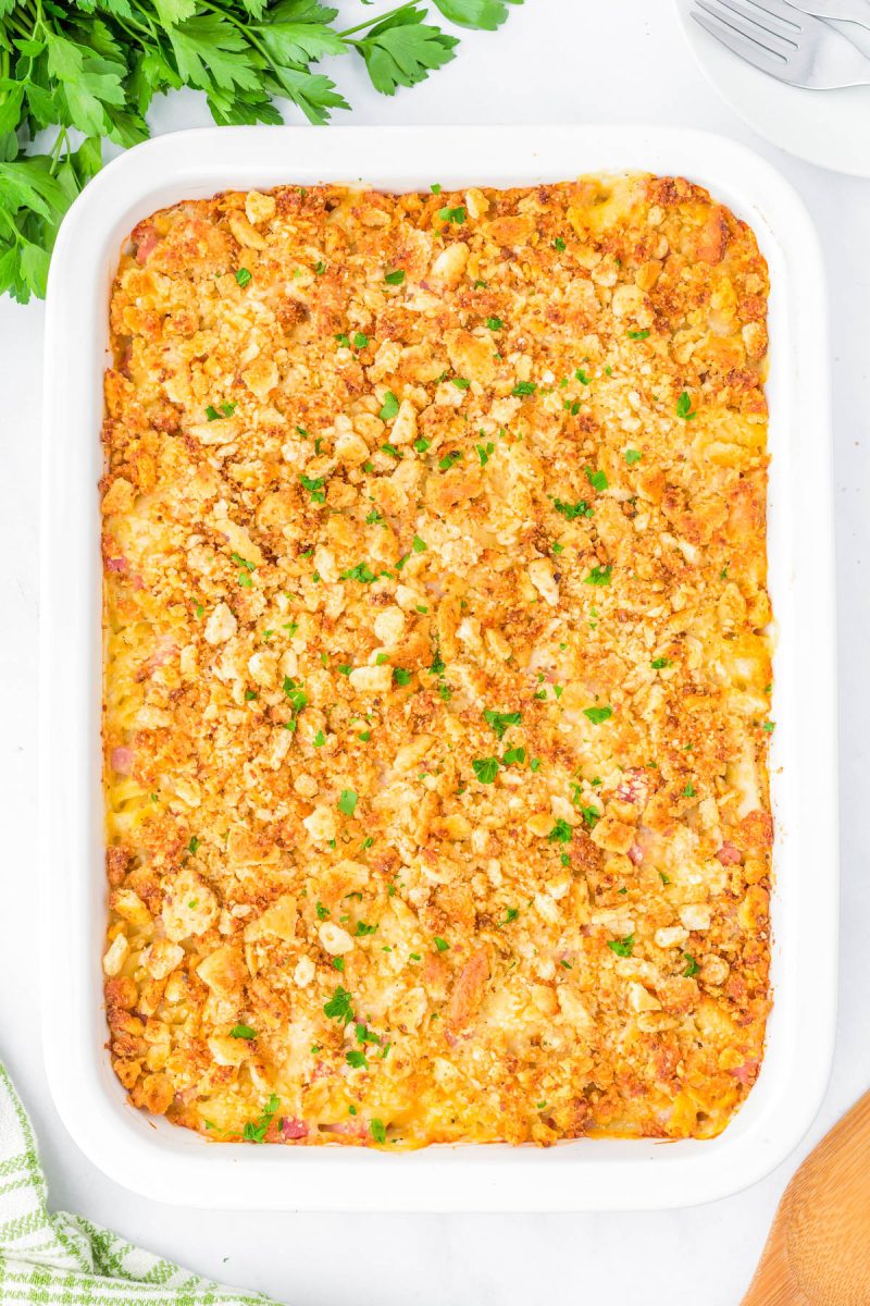 A baked casserole topped with a golden, crispy breadcrumb layer, garnished with chopped parsley in a white rectangular dish.