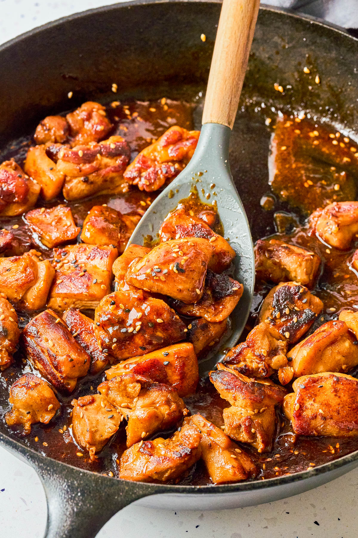 Chunks of cooked chicken in a skillet with brown sauce, being stirred with a gray spatula.