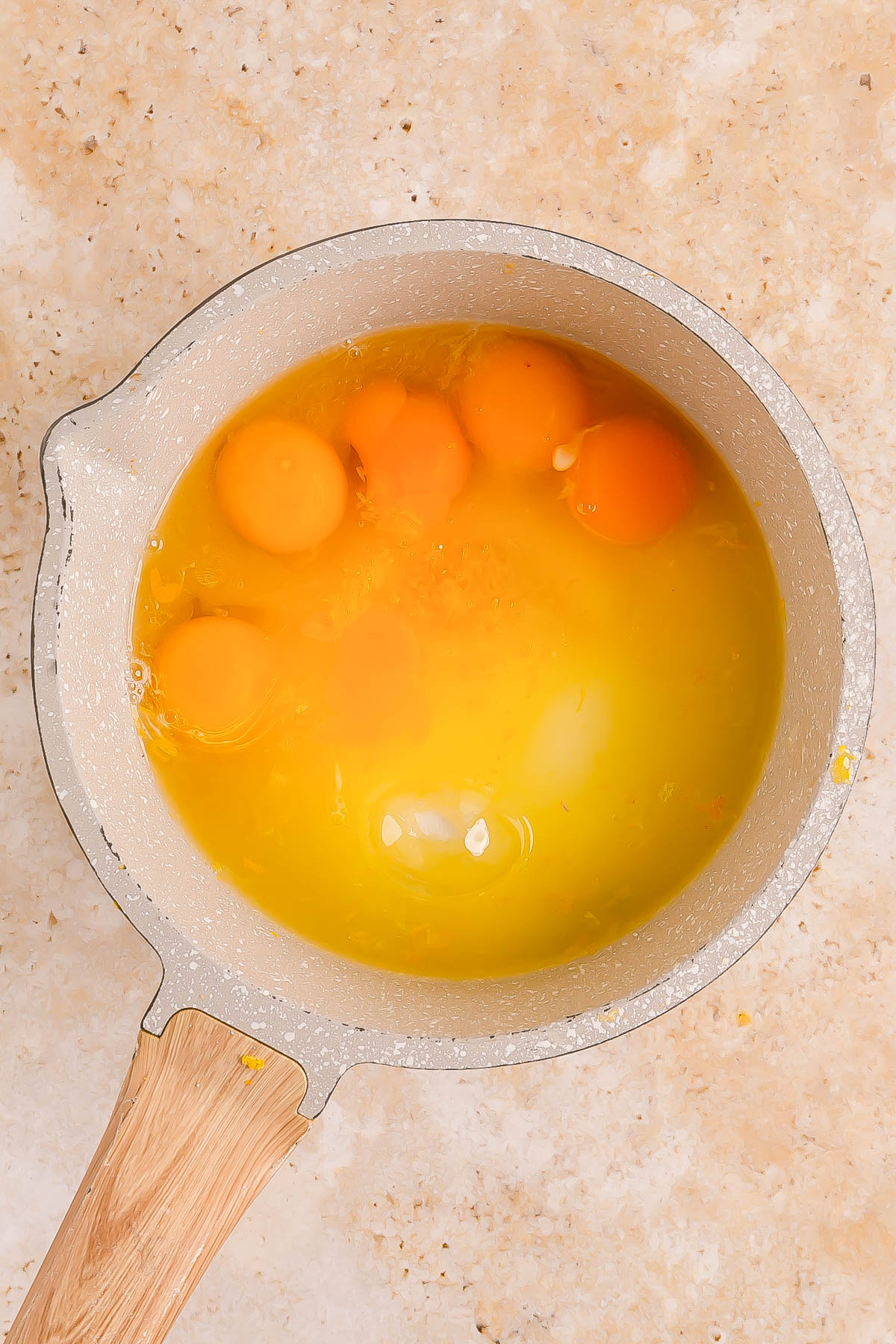 A saucepan containing several cracked raw eggs with intact yolks and whites, placed on a light-colored countertop.