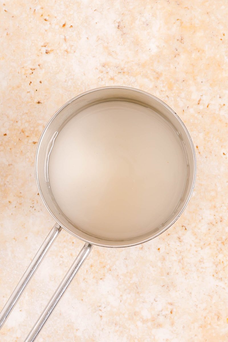 A metal saucepan filled with a clear liquid is placed on a light beige, speckled surface.