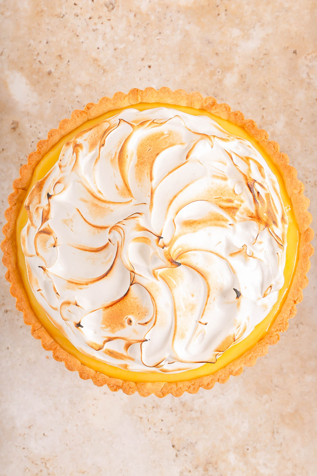 A lemon meringue pie with toasted swirls of meringue on top, seen from above on a light-colored surface.
