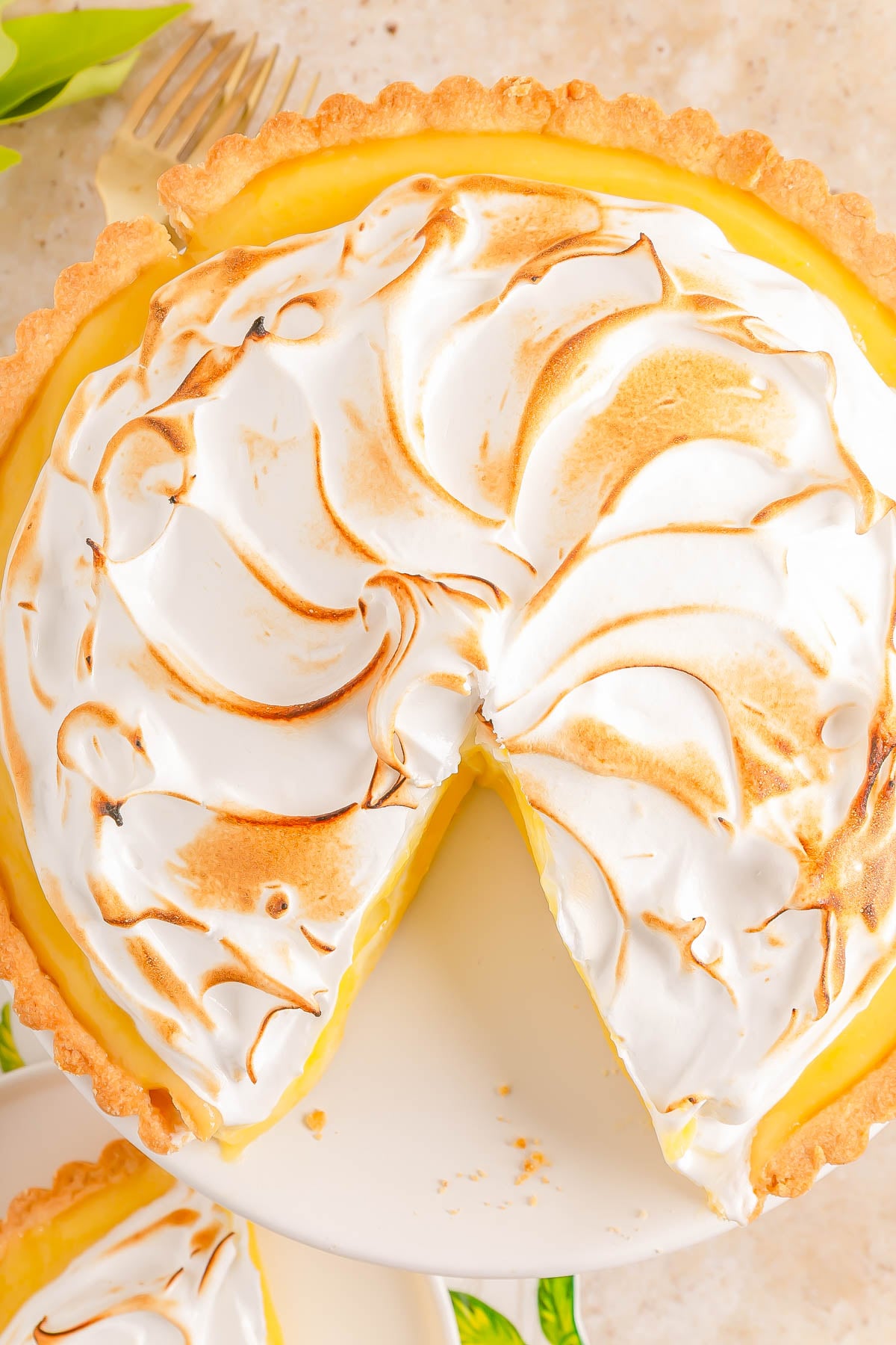 A lemon meringue pie with a slice removed, showing a golden crust, yellow filling, and toasted meringue topping on a white plate.