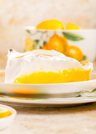 A slice of lemon meringue pie with a golden-yellow filling and fluffy meringue topping sits on a decorative plate.